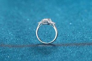 Macro shot of 3ct emerald cut moissanite ring with side stones on blue glitter background