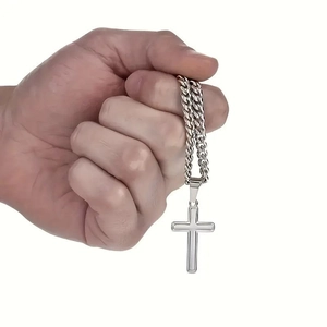 Silver stainless steel cross pendant with Cuban link chain held in hand on white background