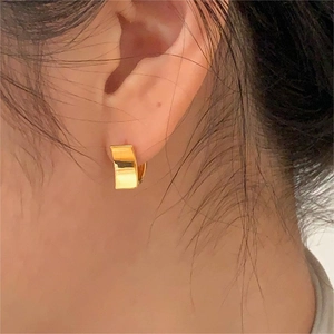 Close-up of elegant gold rectangular brushed earrings worn by a model in warm light