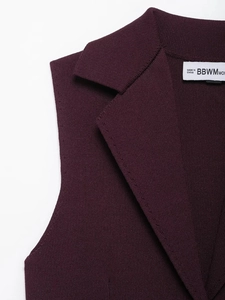 Détail du revers du gilet en maille bordeaux avec étiquette de marque et texture fine