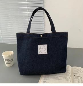 Detail of dark blue denim tote bag featuring a cute white bear patch and retro snap button