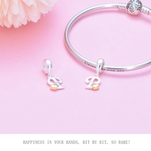 Detail of silver beaded bracelet with letter P charm and golden heart on pink background