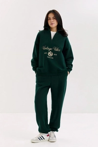 Détail d'un survêtement vert foncé avec sweat à demi-zip et broderie vintage