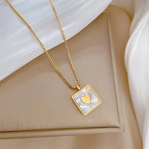 Detailed close-up of a gold square mother-of-pearl pendant with a heart on silk fabric