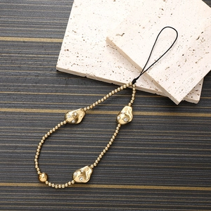Detail of gold beaded phone strap with rhinestone accents on beige textured stone