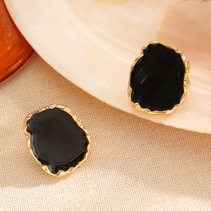 Close-up of vintage irregular golden stud earrings with glossy black enamel inlay