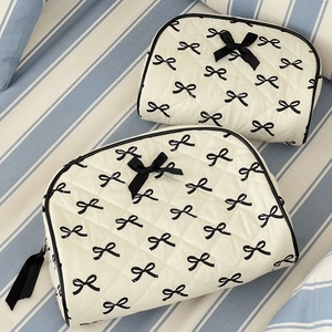 Close-up of two quilted toiletry bags with black bow prints and ribbon zipper details