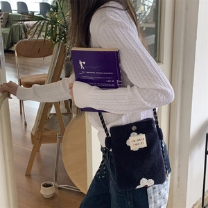 Detail of navy blue plush crossbody bag with white flower patch on model in cafe