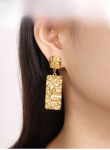 Close-up of golden geometric earrings with irregular lava texture on a model
