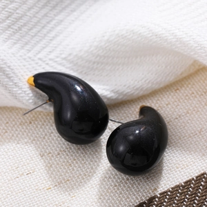 Detail of droplet-shaped black enamel earrings with gold accents on textured fabric