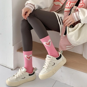 Pink mid-calf socks with white heart and LOVE pattern paired with casual white sneakers