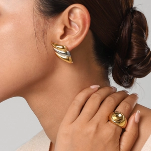 Close-up of stylish two-tone wavy earrings and gold dome ring worn by a model