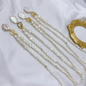 Detail of four Baroque freshwater pearl necklaces with gold T-bar clasps on white silk