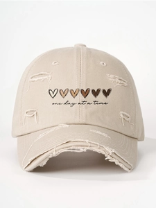 Detail of distressed beige baseball cap with heart prints and one day at a time text