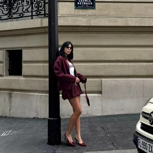 Detail of burgundy jacket suit and skirt outfit worn by a model in an urban street setting