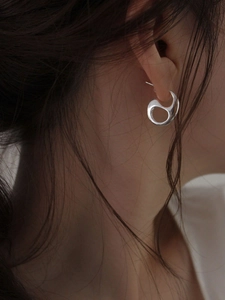 Close-up of polished silver hollow hoop earring on ear with abstract flowing lines