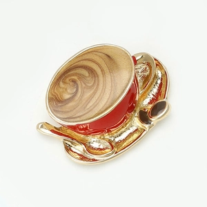 Macro detail of red enamel coffee cup brooch with golden spoon on white background
