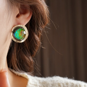 Close-up of a vintage round abalone shell earring with textured gold rim on model ear