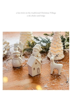 Miniature white glazed ceramic house and snowman Christmas tree ornaments on snow surface