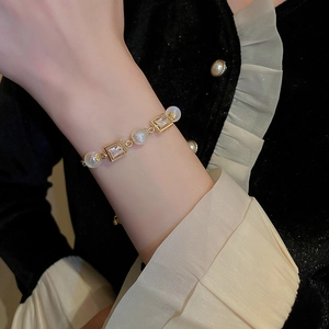 Detail of adjustable gold pearl bracelet with zircon stones on a dark velvet sleeve