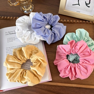 Flat lay of five colorful pleated cotton scrunchies on a wooden tray with a magazine