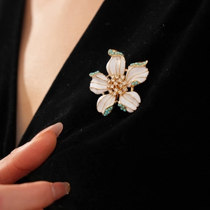 Détail d'une broche fleur en émail blanc avec bords dorés et perles turquoise sur velours