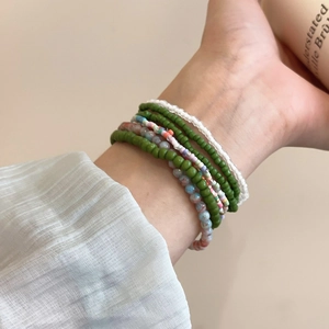 Detail of layered bohemian seed bead bracelets in green and white on a model's wrist