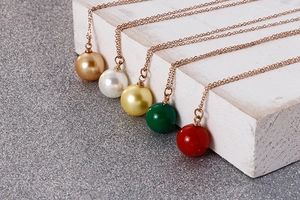 Détail de cinq colliers en acier titane avec perles de nacre colorées en or rose