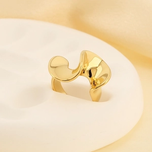 Gros plan d'une bague vague en acier titane doré sur un socle blanc avec tissu doux