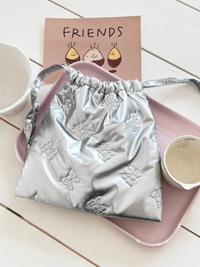 Close-up of silver metallic drawstring pouch with embossed bow patterns on a pink tray