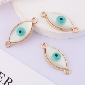 Detailed view of three white evil eye jewelry connectors with gold plating and blue pupils