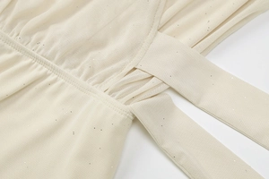Detailaufnahme von Netzstoff mit Pailletten und Bindeband am beigen Wickelkleid