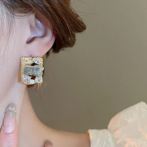 Close-up of vintage gold square earring with crystal and pearl on model's ear