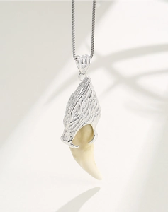 Detailed view of an engraved silver wolf head pendant holding a white tusk on a chain