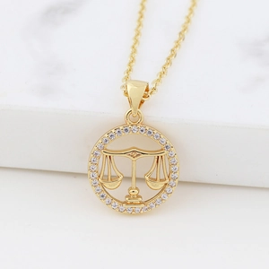 Detail view of gold Libra zodiac necklace with cubic zirconia paving on marble surface