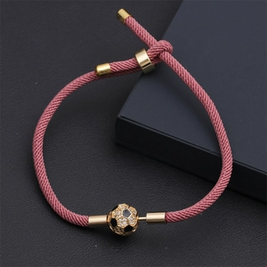 Dettaglio del braccialetto da calcio intrecciato rosa con accenti dorati su fondo nero