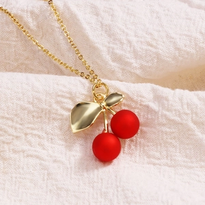 Macro shot of red cherry pendant with golden leaf and thin chain on white fabric