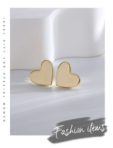 Polished gold heart stud earrings displayed on minimalist white geometric props