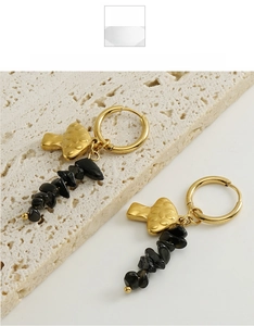 Detail of mushroom pendant gold earrings with black natural stones on a stone tile