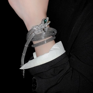 Close-up of a silver snake wrap bracelet with white rhinestones and green gem eyes