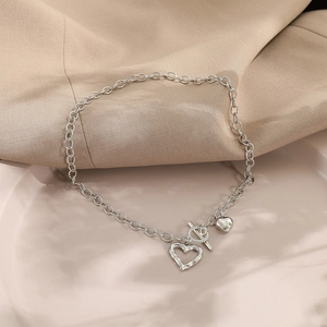 Silver necklace detail featuring hollow and solid heart pendants with a stylish OT toggle clasp