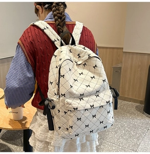 Detailed view of the cream corduroy backpack featuring black bow tie and ribbon details