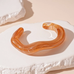 Macro shot of wave-shaped acrylic bangle with amber texture on a white stone pedestal