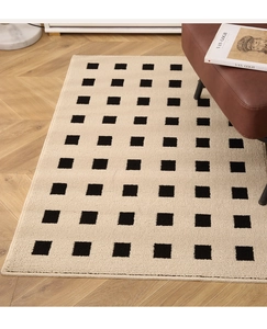 Detail of beige entryway rug with black square patterns on herringbone wood flooring