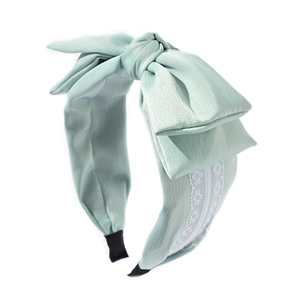 Light green fabric headband with a large bow and white lace trim on a white background