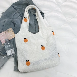 Detail of white faux shearling tote bag with orange fruit embroidery on quilted background
