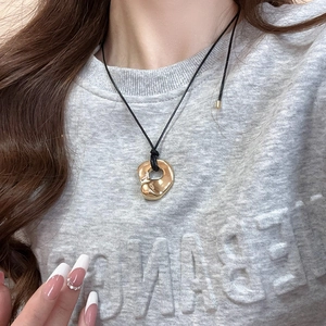 Close-up of gold organic irregular pendant on black cord worn over grey sweatshirt