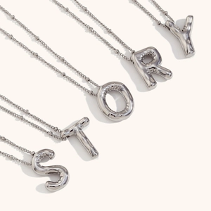 Polished silver balloon letter STORY necklaces in stainless steel on light background
