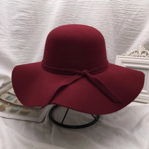 Elegant wine red wide-brimmed wool cloche hat with bow decoration on a metal stand
