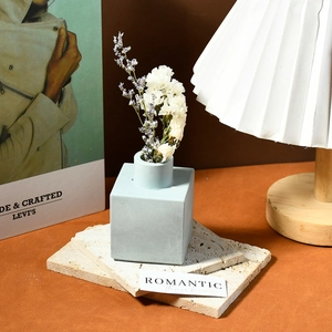 Detail view of square light blue matte vase with dried flowers on a modern stone base